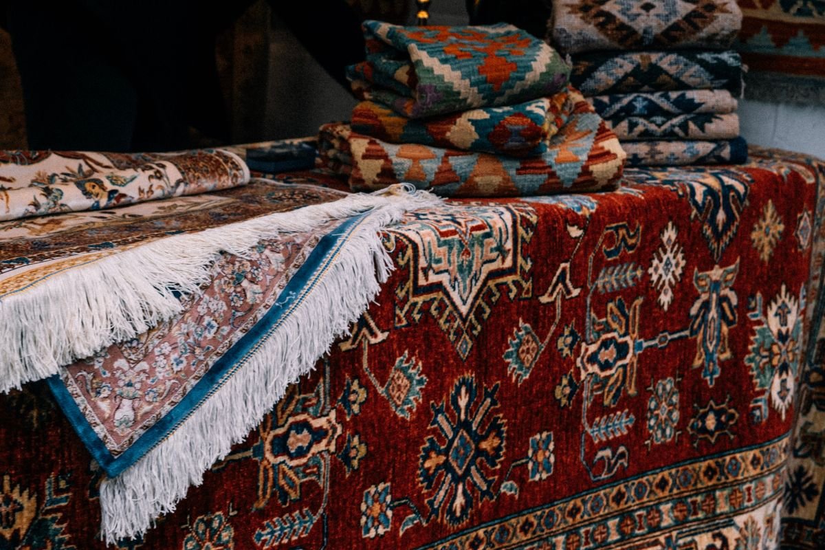 A collection of colorful, intricately patterned rugs displayed on a table, featuring rich reds and detailed designs.